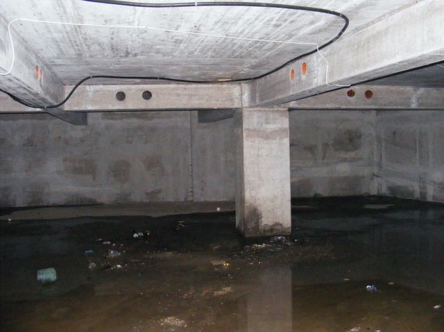 Subsol cu un stâlp de beton care susține grinzi și planșeu, cu apă pe pardoseală.
