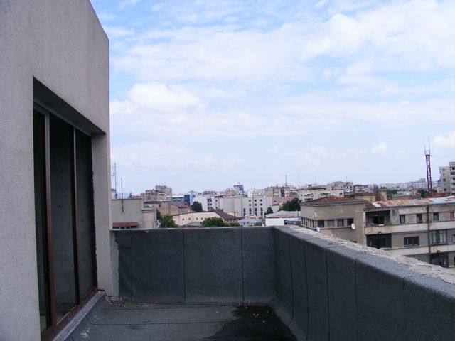 Terasă cu pereți perimetrali și ușă vitrată, cu orașul în fundal.