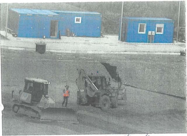 Buldozer și încărcător cu cupă pe suprafața bazei celulei, în spate containere albastre de șantier
