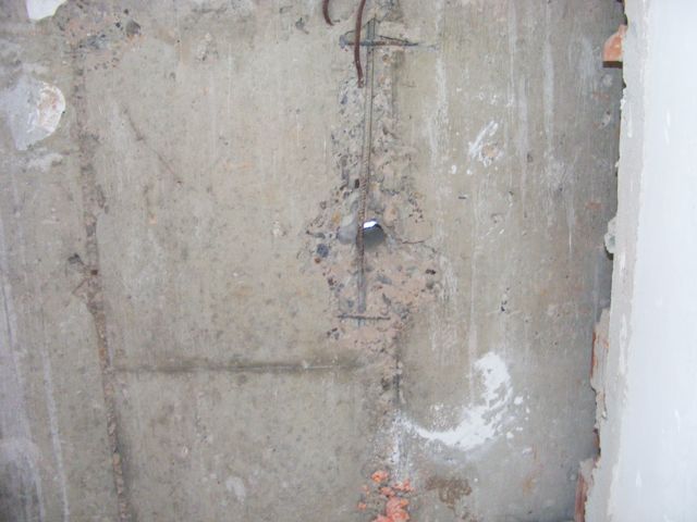 Suprafață de beton cu neuniformități, bară de armătură vizibilă și cărămidă la margine